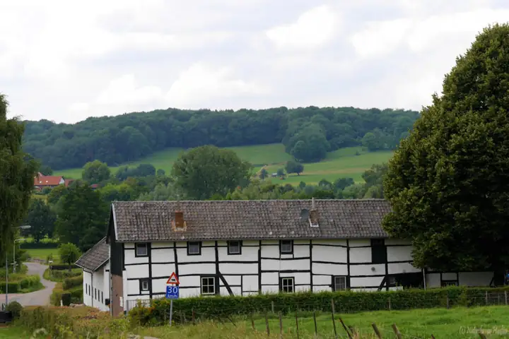 Zwart-witte vakwerkboerderij van Vakantiewoning Hupperetz met de heuvels erachter